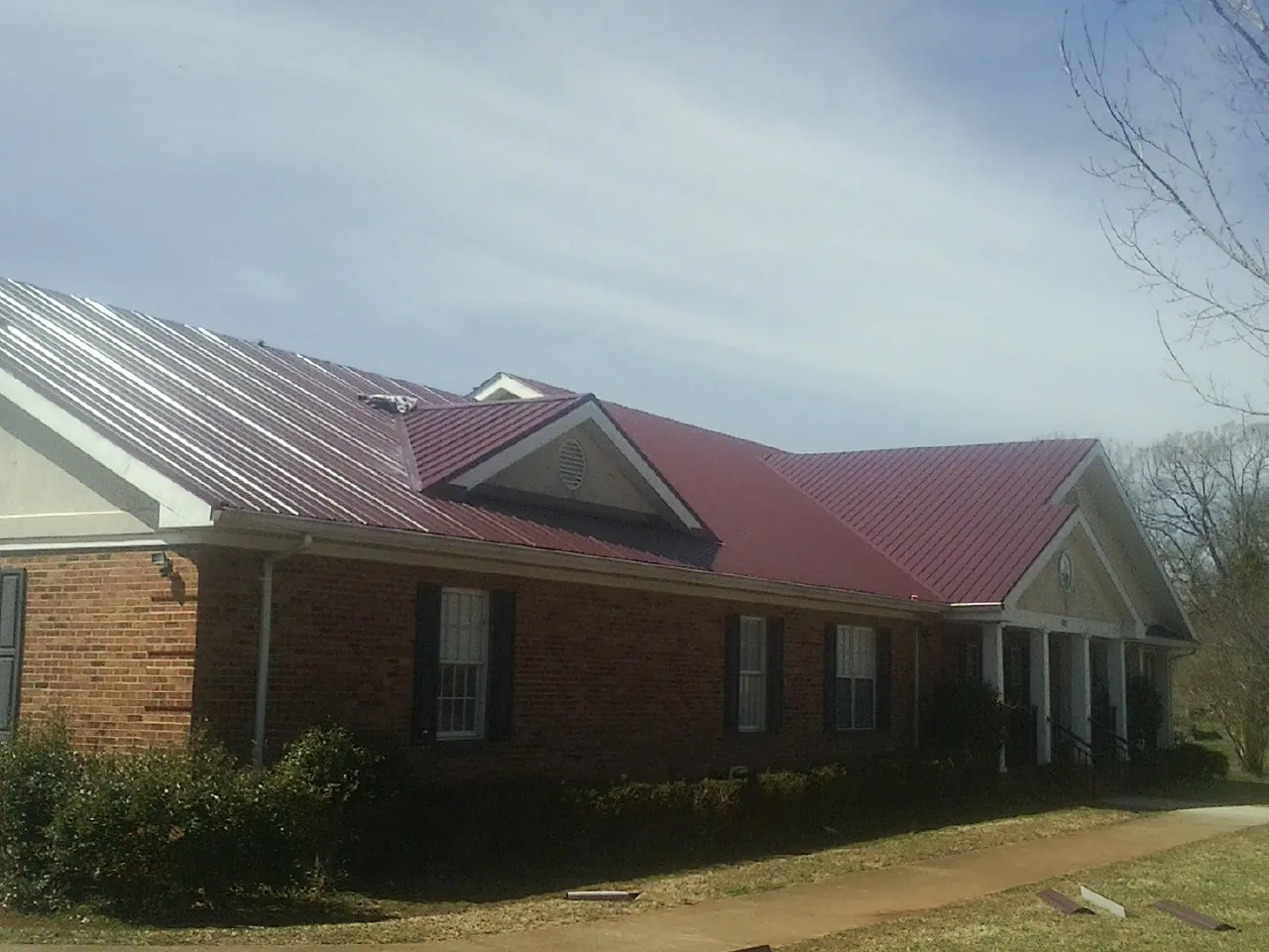 Red metal roof with gabled entries on a long brick building, from a Hail Damage Roof Repair job in Spencerville