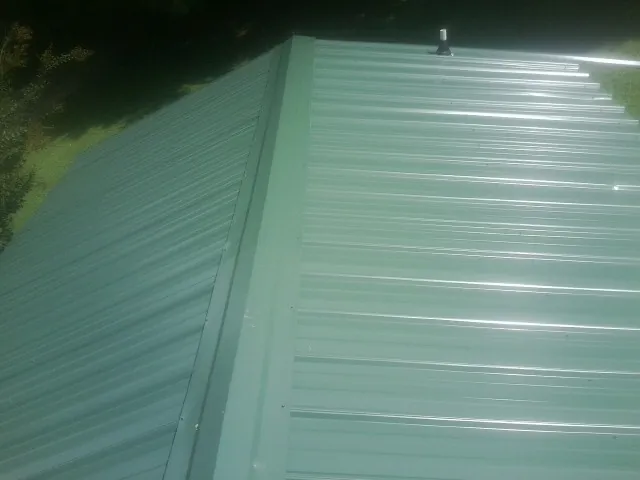 New green metal panels meeting at the ridge of a roof — Flat Roof Repair work by our crew in Spencerville