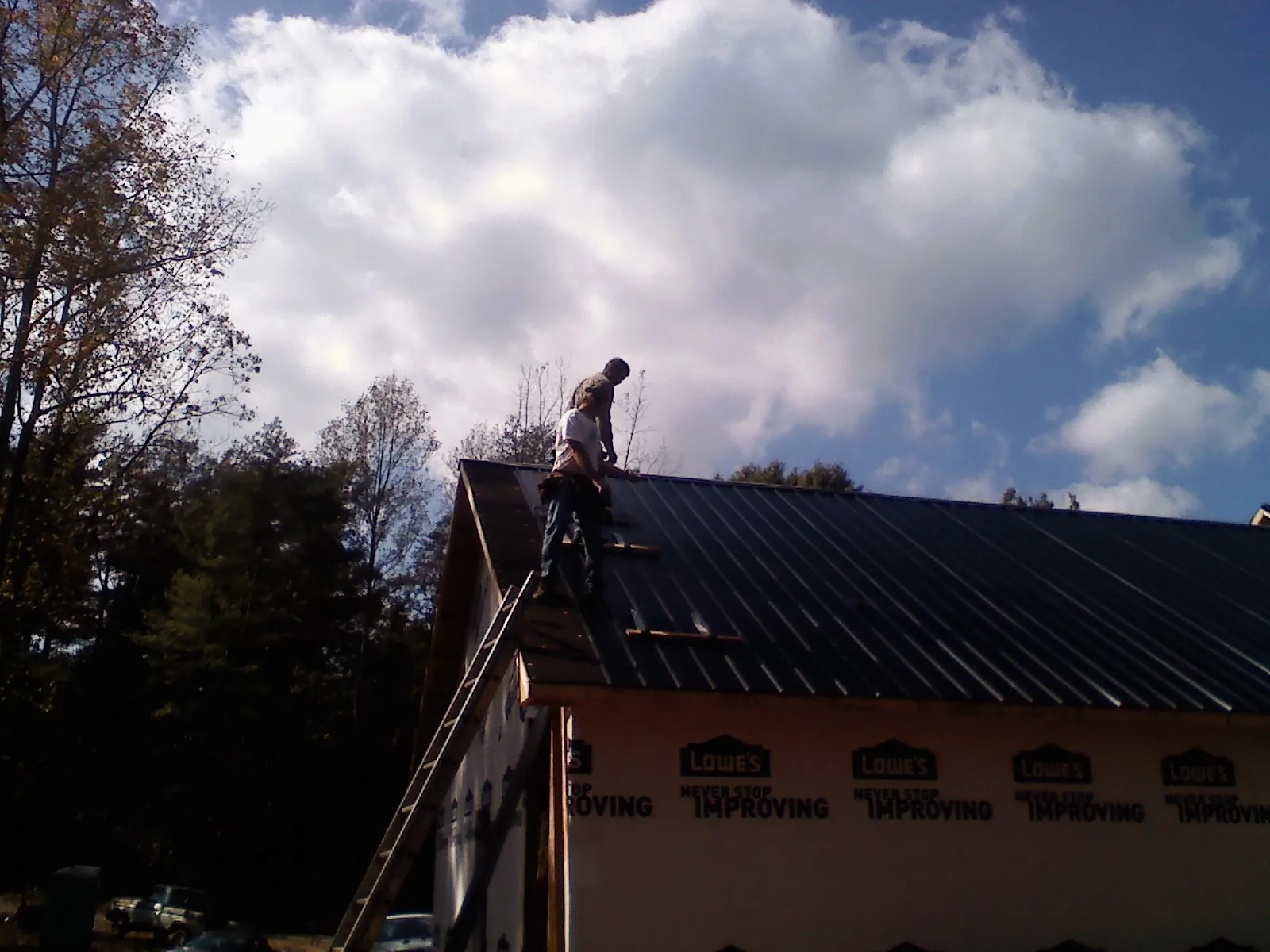 Roofer fastening dark metal panels high against a cloudy sky, from a Roof Inspection job in Spencerville
