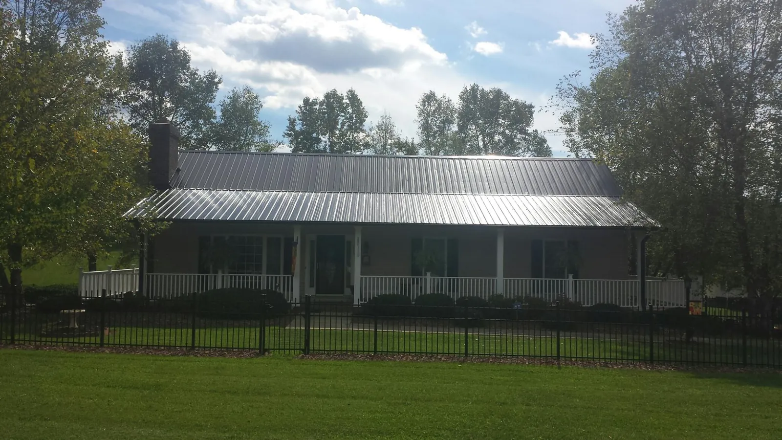 Gray metal roof on a brick ranch with a full width front porch — Gutter Guard Installation work by our crew in Spencerville